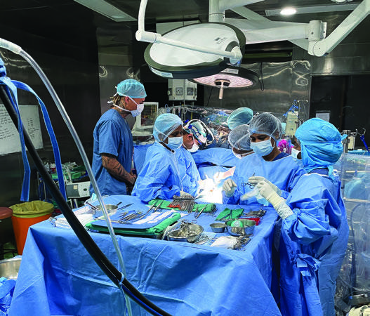 Kenny Stills, standing at the left in blue scrubs, observes the surgical team at Amrita Hospital.